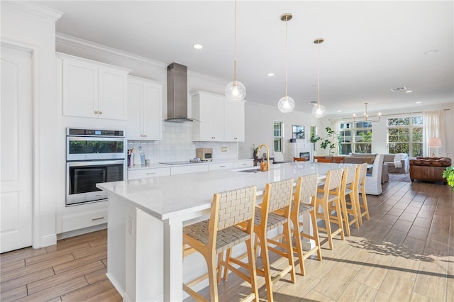 kitchen featuring white cabinetry, a large island, pendant lighting, and wall chimney exhaust hood