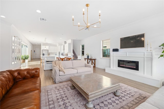 living room with an inviting chandelier, ornamental molding, a healthy amount of sunlight, and light hardwood / wood-style floors