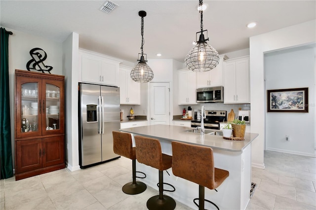 kitchen with a breakfast bar area, white cabinetry, decorative light fixtures, a center island with sink, and appliances with stainless steel finishes