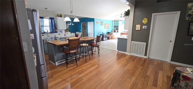 kitchen featuring white cabinetry, sink, wooden counters, a kitchen breakfast bar, and hanging light fixtures