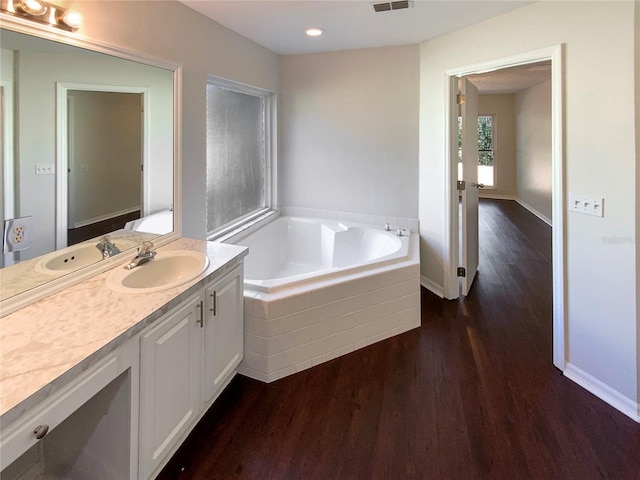 bathroom featuring hardwood / wood-style flooring, vanity, and tiled bath