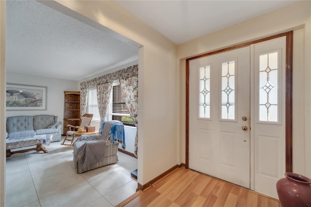 entryway with light wood finished floors, baseboards, and a textured ceiling