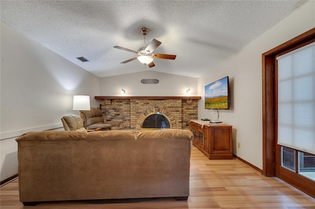 living area featuring ceiling fan, visible vents, light wood-style floors, vaulted ceiling, and a brick fireplace