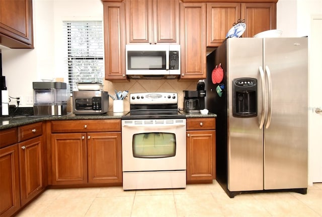 kitchen with light tile patterned flooring, appliances with stainless steel finishes, decorative backsplash, and dark stone counters