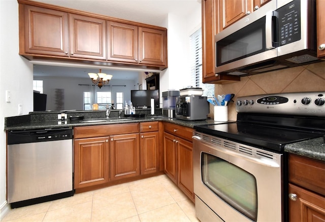 kitchen with sink, dark stone counters, light tile patterned floors, a notable chandelier, and stainless steel appliances