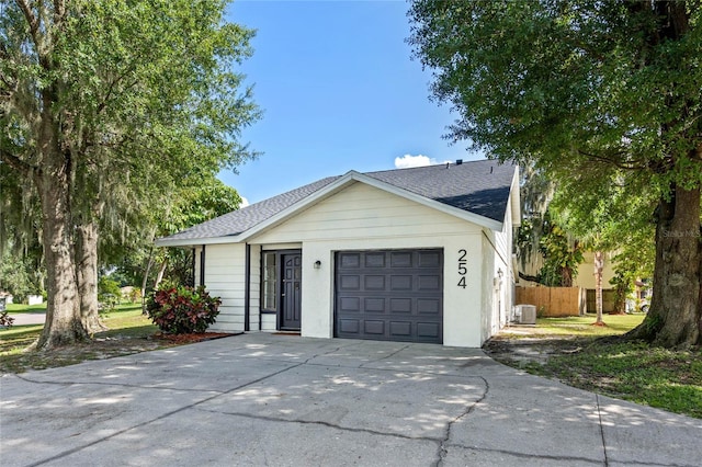 ranch-style house with driveway, central AC unit, roof with shingles, an attached garage, and fence