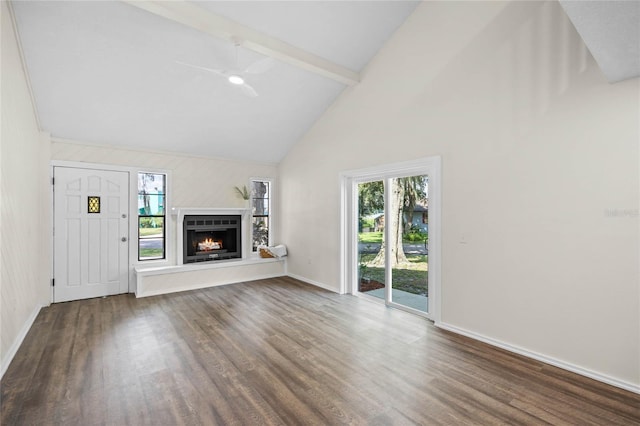 unfurnished living room with wood finished floors, a ceiling fan, baseboards, a lit fireplace, and beam ceiling