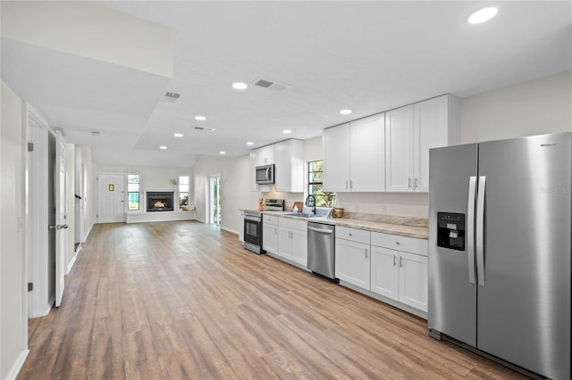 kitchen with stainless steel appliances, light countertops, light wood-style floors, white cabinetry, and a sink