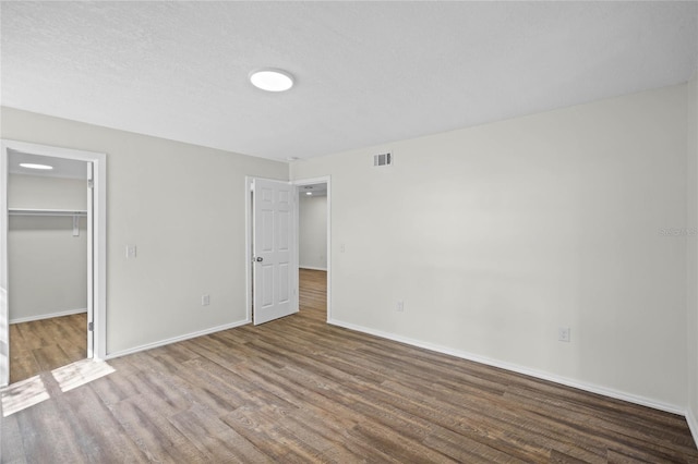 unfurnished bedroom with wood finished floors, visible vents, baseboards, a spacious closet, and a closet