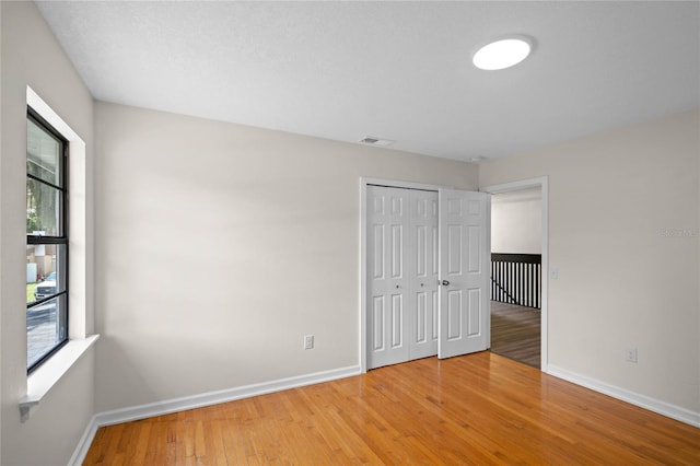 unfurnished bedroom with a closet, wood-type flooring, visible vents, and baseboards