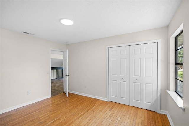 unfurnished bedroom with a closet, visible vents, light wood-style flooring, and baseboards