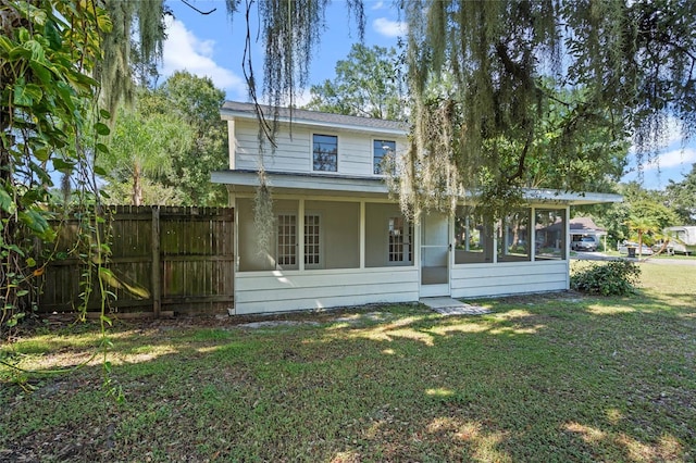 back of property with a sunroom, a lawn, and fence