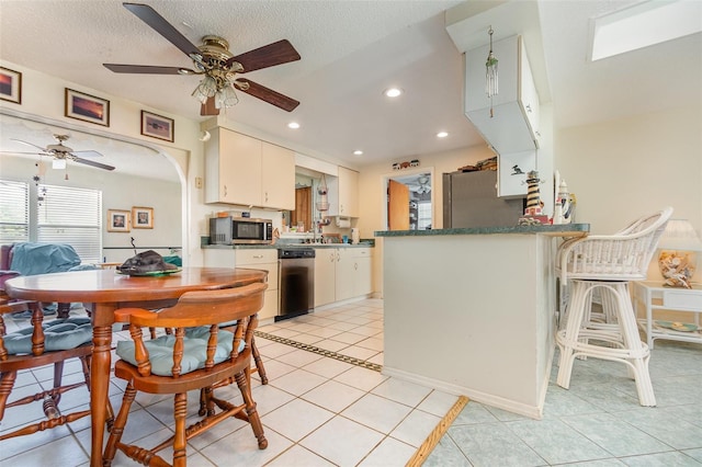 kitchen with arched walkways, light tile patterned floors, stainless steel appliances, dark countertops, and white cabinets