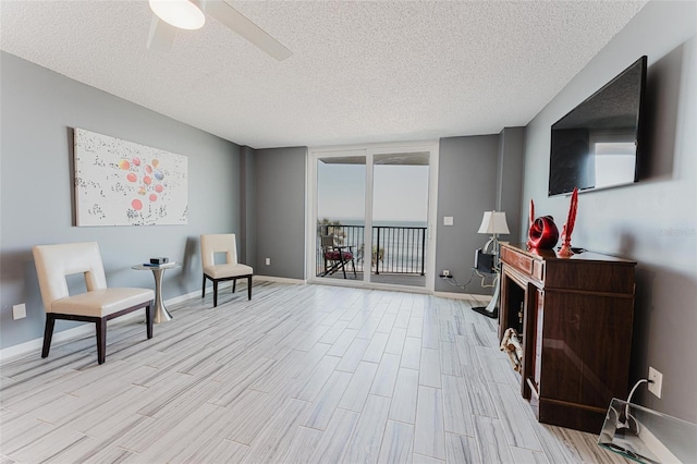 living area featuring ceiling fan, light hardwood / wood-style floors, and a textured ceiling