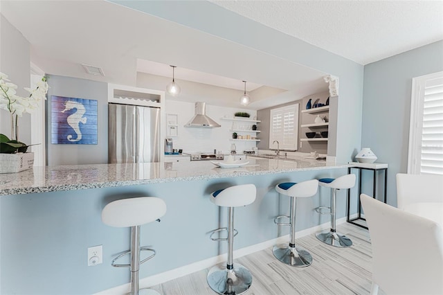 kitchen featuring pendant lighting, stainless steel fridge, a kitchen breakfast bar, and wall chimney exhaust hood