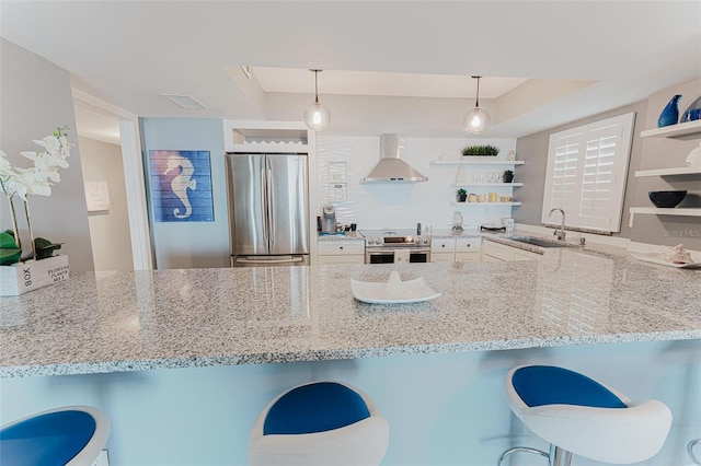 kitchen featuring a kitchen bar, sink, decorative light fixtures, stainless steel appliances, and wall chimney range hood