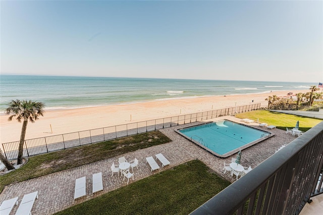 view of swimming pool with a water view, a beach view, and a lawn