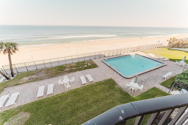 view of swimming pool with a water view, a beach view, and a lawn