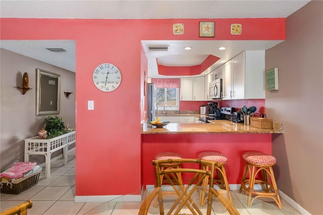 kitchen with appliances with stainless steel finishes, a breakfast bar area, white cabinets, light tile patterned floors, and kitchen peninsula