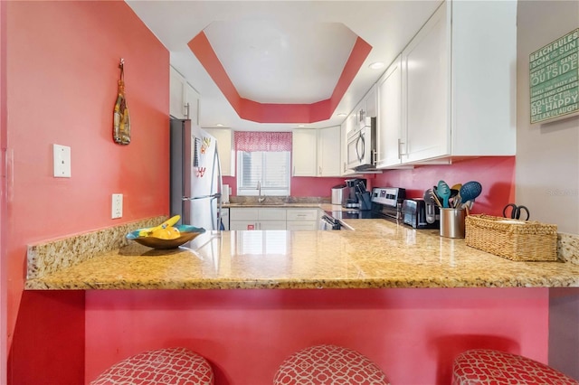 kitchen featuring stainless steel appliances, light stone counters, white cabinets, a kitchen bar, and kitchen peninsula