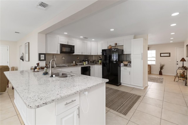 kitchen featuring light tile patterned flooring, light stone countertops, white cabinets, and black appliances