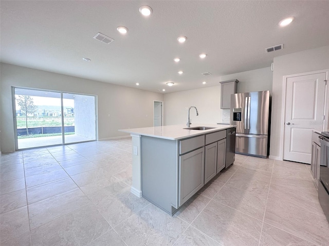 kitchen featuring a kitchen island with sink, sink, gray cabinets, and stainless steel appliances