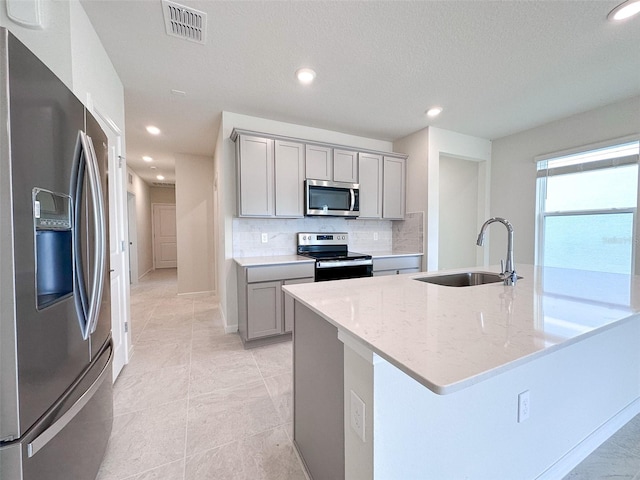 kitchen featuring sink, gray cabinetry, stainless steel appliances, light stone countertops, and decorative backsplash