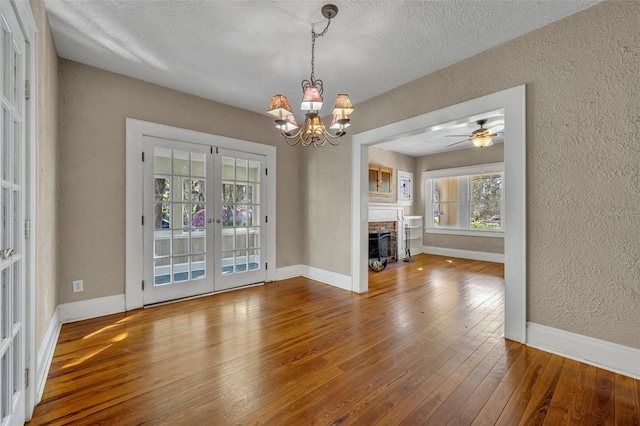 unfurnished dining area featuring french doors, a textured wall, a brick fireplace, baseboards, and hardwood / wood-style flooring