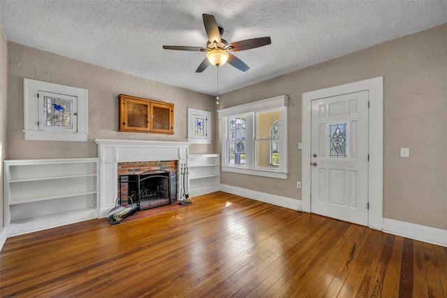 unfurnished living room featuring a fireplace, a textured wall, baseboards, and hardwood / wood-style flooring