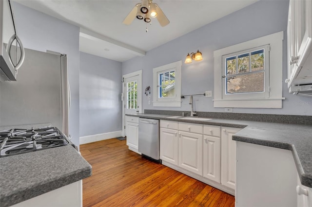 kitchen with a sink, white cabinetry, appliances with stainless steel finishes, light wood finished floors, and dark countertops