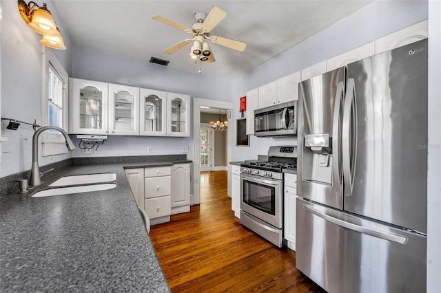 kitchen featuring stainless steel appliances, dark countertops, dark wood-type flooring, white cabinets, and a sink