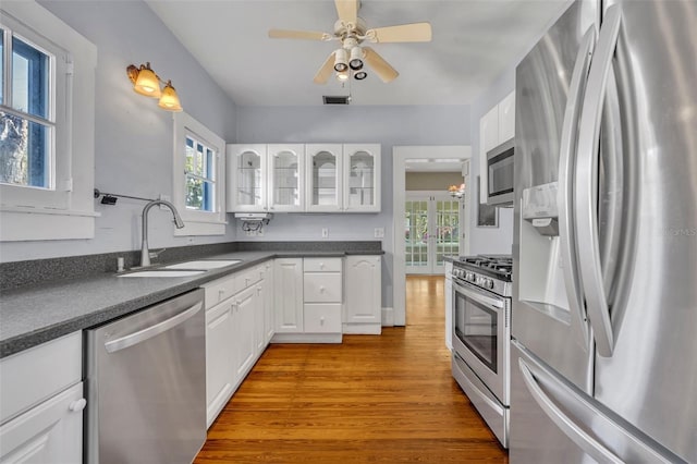 kitchen with a sink, visible vents, appliances with stainless steel finishes, dark countertops, and glass insert cabinets