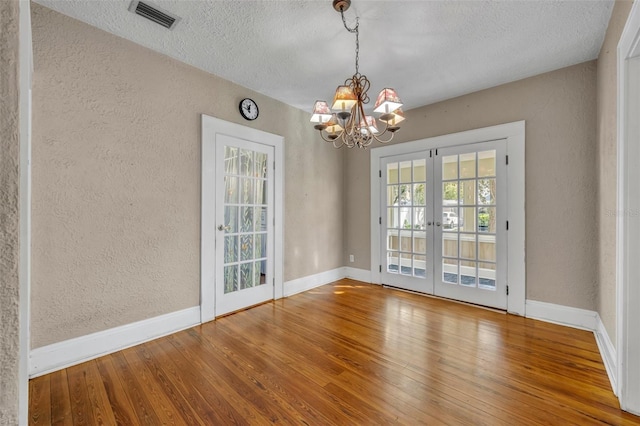 interior space with french doors, visible vents, a textured wall, baseboards, and hardwood / wood-style flooring