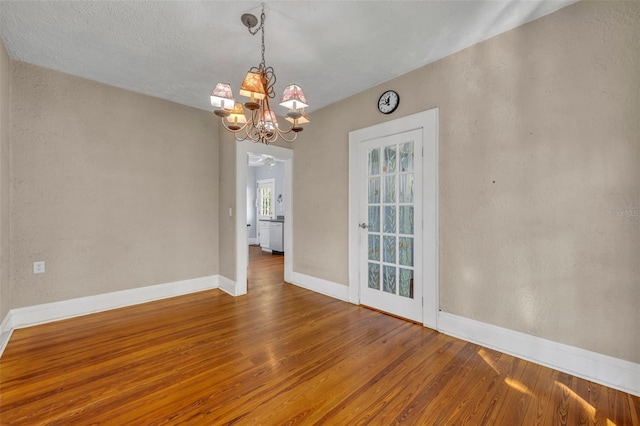 unfurnished room with a textured wall, baseboards, and wood finished floors