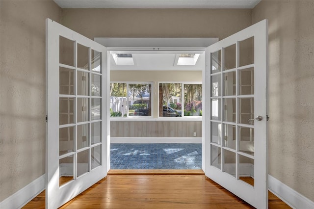 entryway featuring a skylight, wood-type flooring, baseboards, and french doors