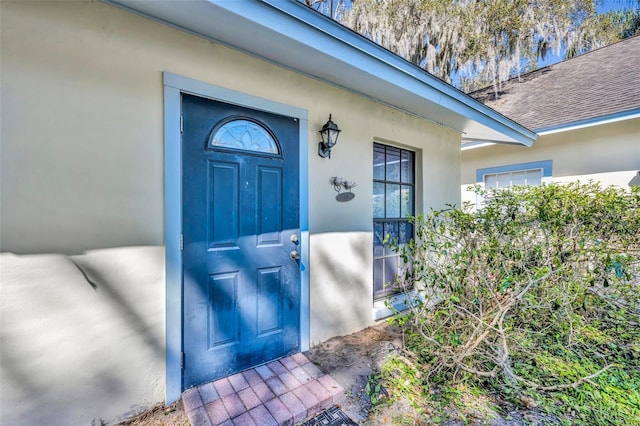 doorway to property with a shingled roof and stucco siding