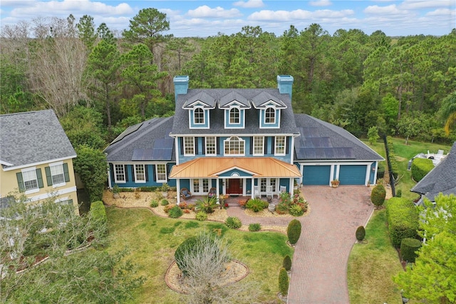 view of front facade featuring decorative driveway, a chimney, solar panels, covered porch, and a front lawn