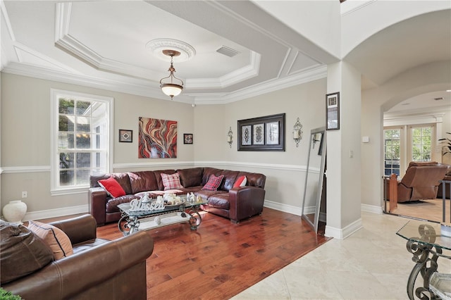 living area featuring arched walkways, a tray ceiling, visible vents, ornamental molding, and baseboards