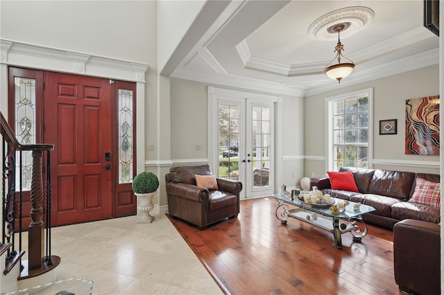 entryway with wood finished floors, stairs, ornamental molding, french doors, and a raised ceiling