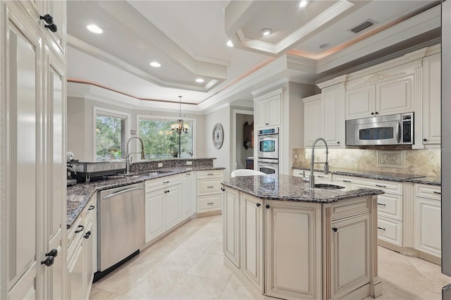 kitchen featuring a sink, visible vents, appliances with stainless steel finishes, a tray ceiling, and an island with sink