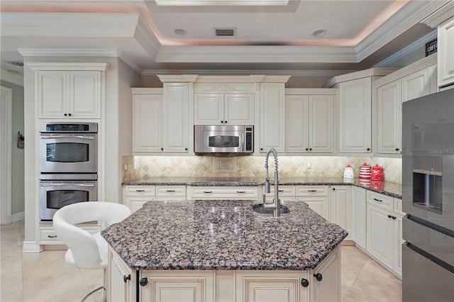 kitchen with appliances with stainless steel finishes, dark stone countertops, a kitchen island with sink, crown molding, and a sink