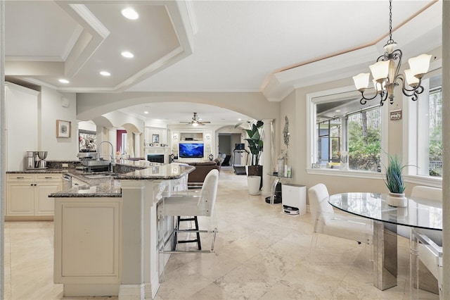 kitchen featuring arched walkways, open floor plan, dark stone counters, decorative light fixtures, and crown molding