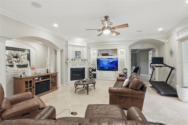 living area featuring decorative columns, arched walkways, a glass covered fireplace, crown molding, and built in shelves