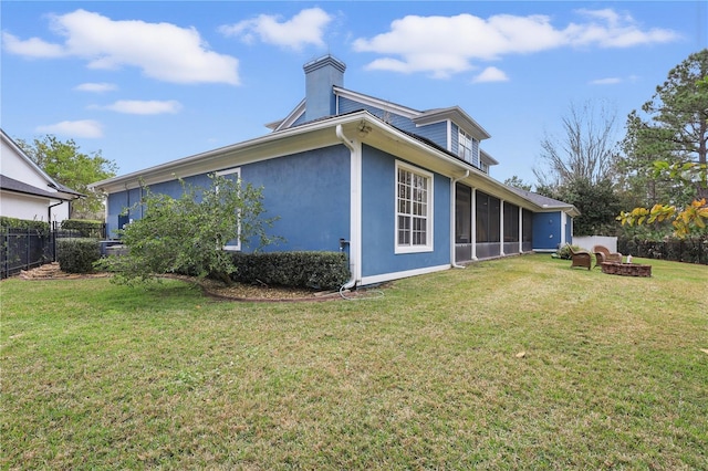 rear view of property featuring a fire pit, a lawn, fence, and a sunroom