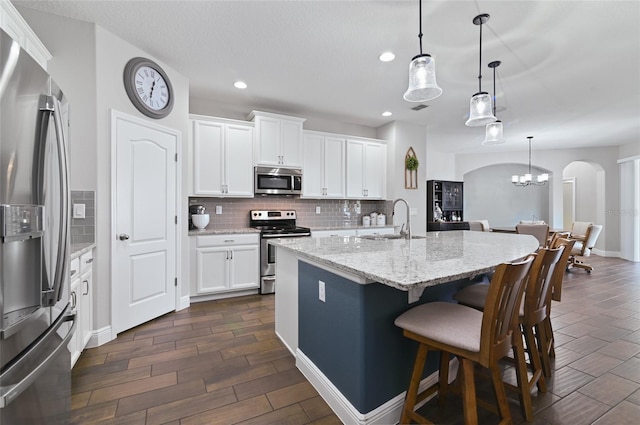 kitchen featuring appliances with stainless steel finishes, an island with sink, sink, white cabinets, and hanging light fixtures