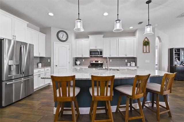 kitchen featuring white cabinetry, appliances with stainless steel finishes, hanging light fixtures, and a center island with sink