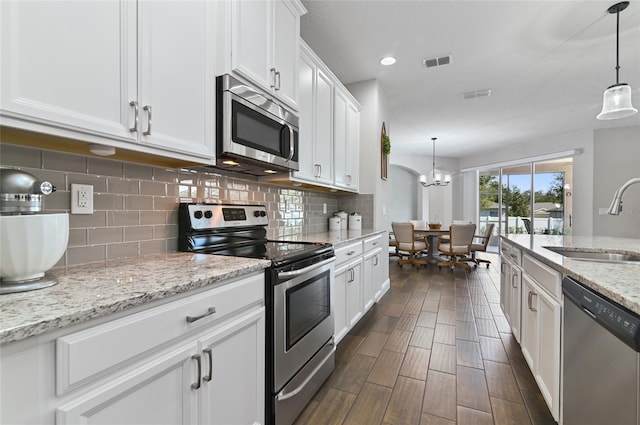 kitchen with appliances with stainless steel finishes, pendant lighting, sink, white cabinets, and light stone counters