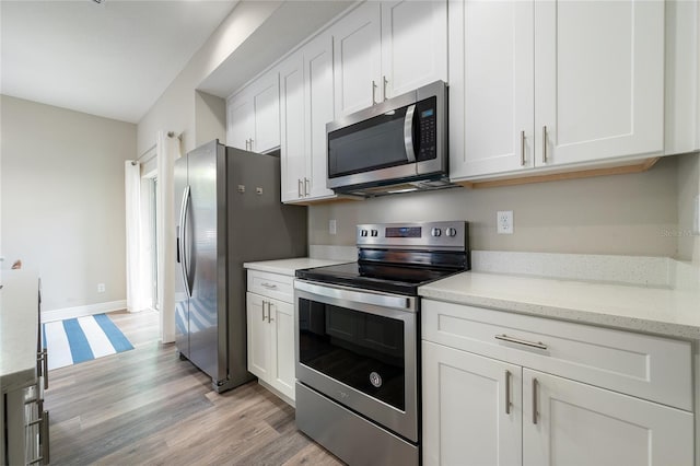 kitchen with light stone countertops, white cabinetry, appliances with stainless steel finishes, and light hardwood / wood-style floors