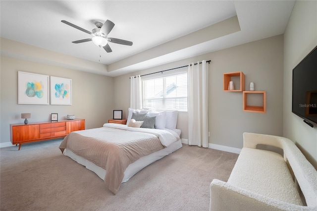 bedroom with ceiling fan, light colored carpet, and a tray ceiling