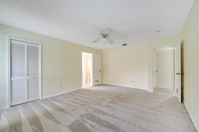 unfurnished bedroom with ceiling fan, connected bathroom, a textured ceiling, light carpet, and a closet